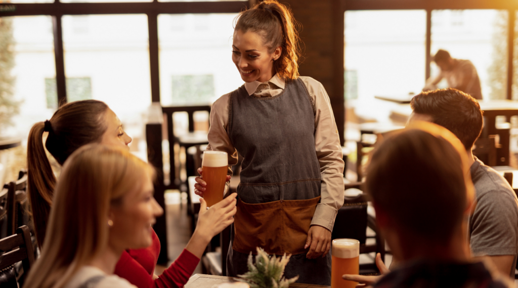 Happy waitress serving beer to group of customers