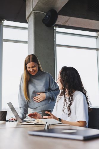 Two young women work in a modern office. Work office space with large windows. Woman manager works at the desk sitting in the office.